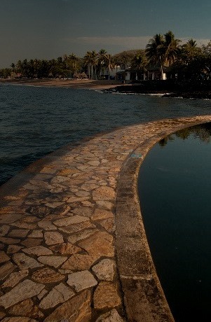 A rock path separates the sea from a salt water pool in El Salvador